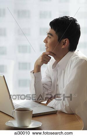 Young man sitting with laptop looking out window View Large Photo Image Stock Image - Young man sitting with laptop looking out window. Fotosearch