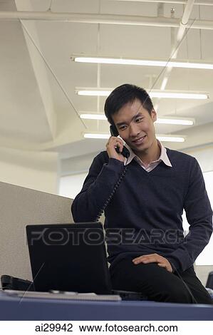 Stock Image - Young man talking on phone and working on computer. Fotosearch