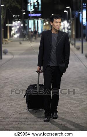 Young man walking down a street pulling a suitcase View Large Photo Image Picture - Young man walking down a street pulling a suitcase. Fotosearch