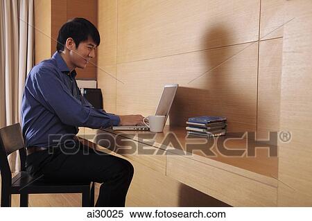 Stock Photography - Young man working on a laptop computer at home. Fotosearch