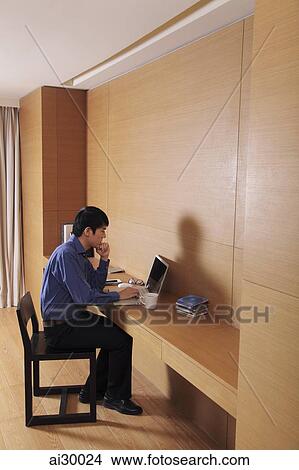 Picture - Young man working on laptop at home. Fotosearch