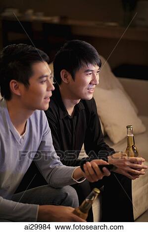 Young men watching TV and holding bottles of beer View Large Photo Image Picture - Young men watching TV and holding bottles of beer. Fotosearch