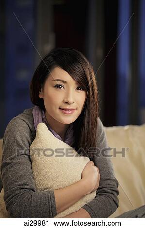 Stock Image - Young woman holding a pillow and smiling. Fotosearch
