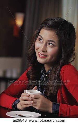 Stock Image - Young woman holding coffee cup and looking up. Fotosearch