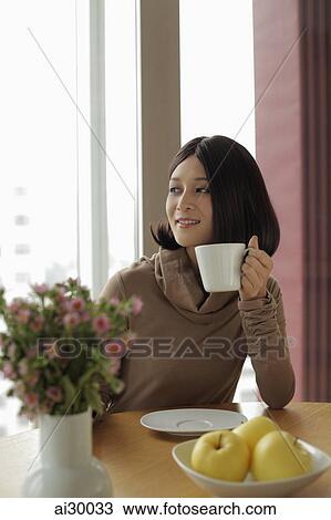 Young woman holding coffee looking out the window View Large Photo Image Stock Image - Young woman holding coffee looking out the window. Fotosearch