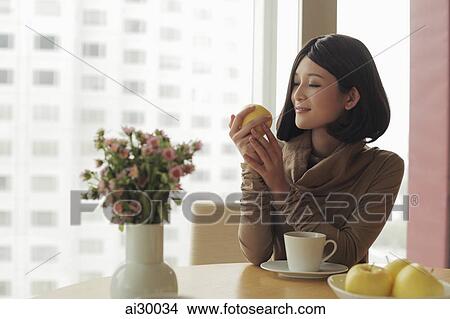 Picture - Young woman looking at apple and smiling. Fotosearch