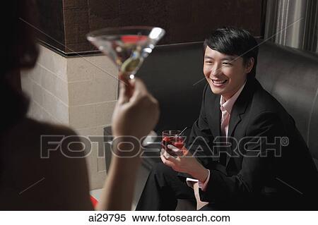 Stock Photography - Young woman looking at young man holding a drink and smiling. Fotosearch