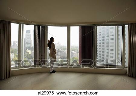 Stock Photography - Young woman looking out large windows of condo. Fotosearch