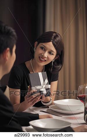 Young woman opening a present during a romantic dinner View Large Photo Image Stock Image - Young woman opening a present during a romantic dinner. Fotosearch