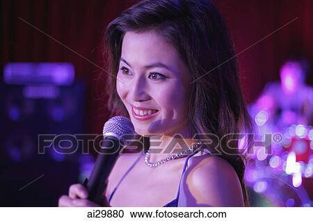 Young woman singing into a microphone at night View Large Photo Image Stock Image - Young woman singing into a microphone at night. Fotosearch