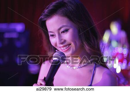 Young woman singing into a microphone at night View Large Photo Image Stock Photo - Young woman singing into a microphone at night. Fotosearch