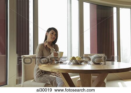 Young woman sitting at a table drinking tea View Large Photo Image Stock Photo - Young woman sitting at a table drinking tea. Fotosearch