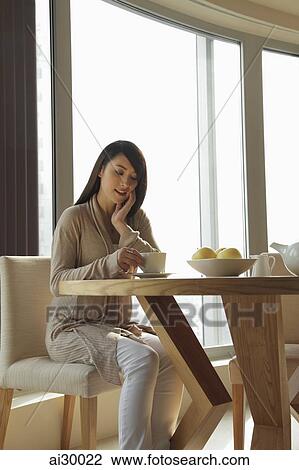 Stock Image - Young woman sitting at a table looking down. Fotosearch