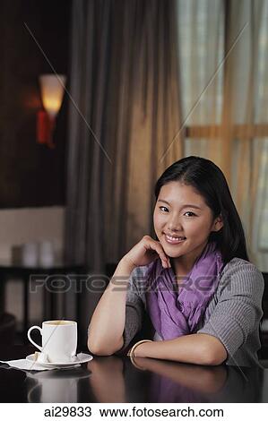 Stock Image - Young woman sitting in cafe with coffee cup. Fotosearch