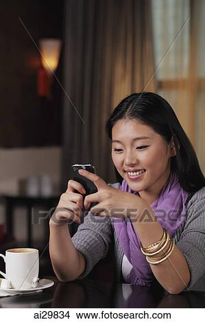 Picture - Young woman sitting in restaurant holding phone. Fotosearch