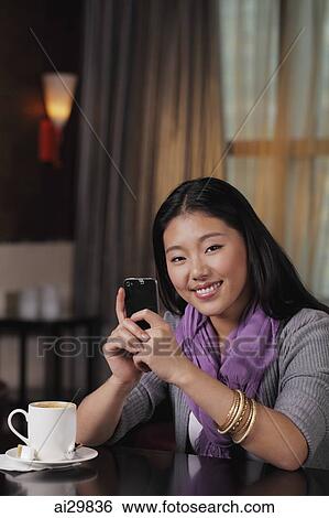 Stock Photograph - Young woman sitting in restaurant holding phone. Fotosearch