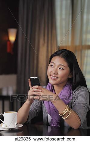 Young woman sitting in restaurant holding phone View Large Photo Image Stock Photography - Young woman sitting in restaurant holding phone. Fotosearch