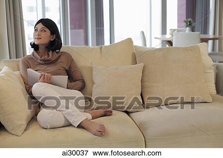 Stock Photo - Young woman sitting on sofa in living room. Fotosearch