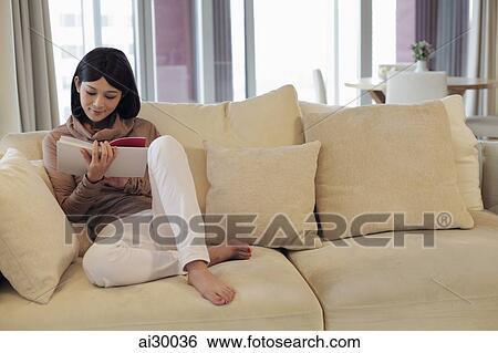 Young woman sitting on sofa reading a book in living room View Large Photo Image Stock Photograph - Young woman sitting on sofa reading a book in living room. Fotosearch