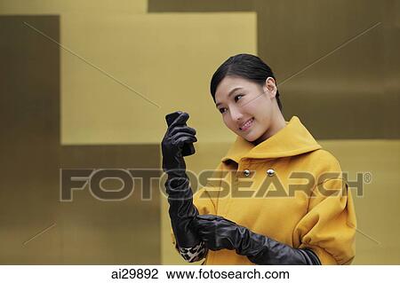 Stock Image - Young woman wearing black gloves looking at phone. Fotosearch
