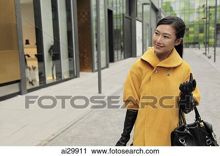 Stock Image - Young woman wearing coat and gloves, shopping outdoors. Fotosearch
