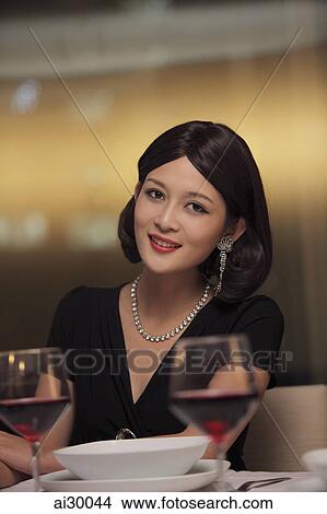 Picture - Young woman wearing diamond jewelry sitting at table. Fotosearch