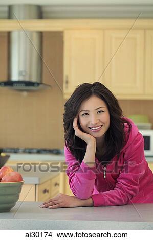 Picture - Young woman wearing pink smiling in her kitchen. Fotosearch
