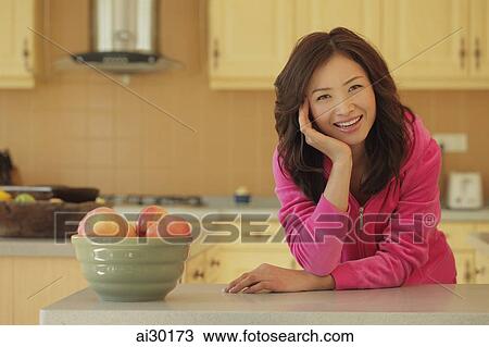 Stock Image - Young woman wearing pink smiling in her kitchen. Fotosearch