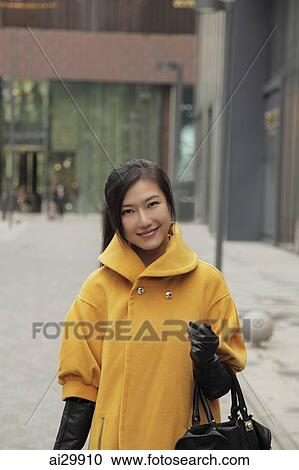 Stock Image - Young woman wearing yellow coat and gloves shopping outdoors. Fotosearch