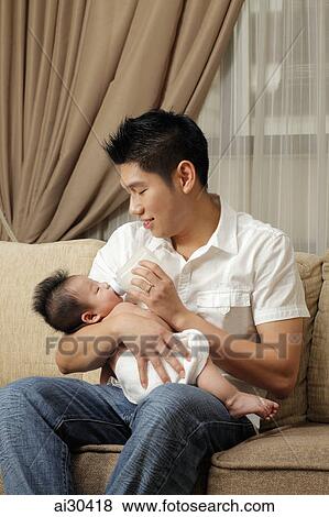Stock Photo - A father gives his baby a bottle of milk. Fotosearch