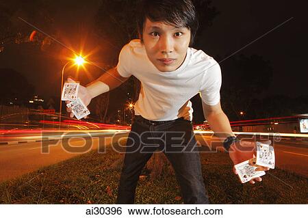 Stock Photograph - A man holding playing cards on the street at night. Fotosearch