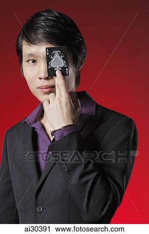 Stock Image - A man holds a card with the Ace of Spades in front of his eye. Fotosearch