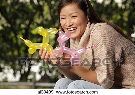 Stock Photo - A woman holds two balloon animals and smiles. Fotosearch