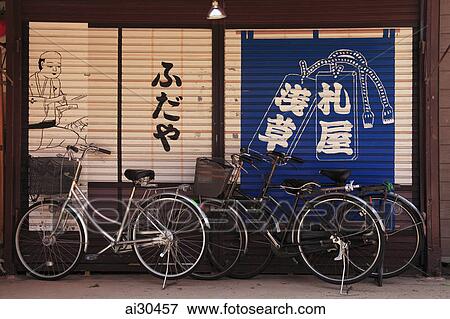 Stock Photo - Bicycles parked against a wall with Japanese characters and art, Japan. Fotosearch