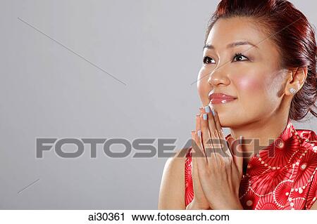 Stock Image - Head shot of woman with hands together looking up. Fotosearch