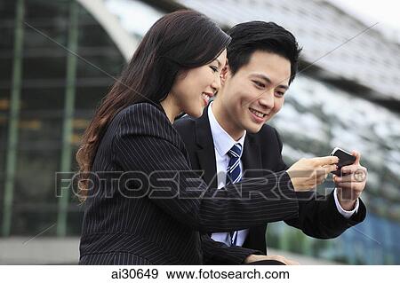 Stock Photo - Man and woman wearing business attire looking at a phone together. Fotosearch