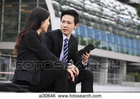 Man and woman wearing business attire talking over a digital tablet View Large Photo Image Stock Photograph - Man and woman wearing business attire talking over a digital tablet. Fotosearch