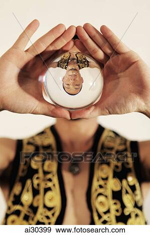 Stock Photo - Man holding crystal ball in front of his face with his reflection upside down. Fotosearch