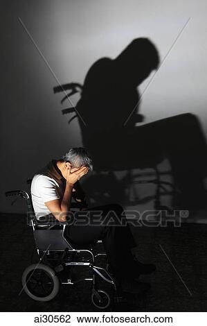 Man sitting in a wheelchair with head in hands with dramatic shadow on the wall View Large Photo Image Stock Image - Man sitting in a wheelchair with head in hands with dramatic shadow on the wall. Fotosearch