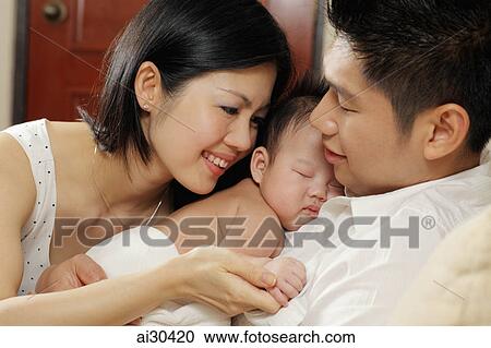 Stock Image - Mother and father holding their sleeping baby. Fotosearch