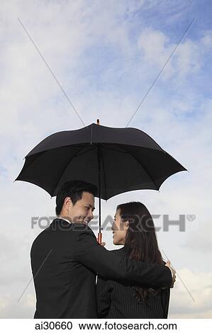 Rear view of couple holding a black umbrella smiling at each other. View Large Photo Image Stock Image - Rear view of couple holding a black umbrella smiling at each other.. Fotosearch
