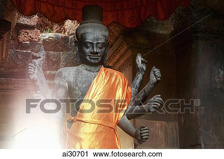 Stock Image - Stone Buddha draped in gold fabric inside a temple, Angkor Wat, Cambodia. Fotosearch