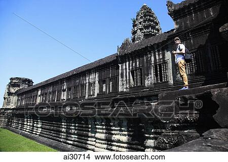 Picture - Tourist standing on the steps of a temple in Angkor Wat, Cambodia. Fotosearch