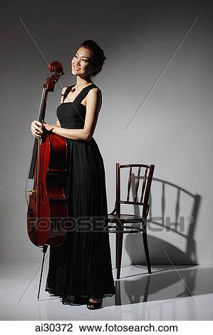 Stock Image - Woman in long black dress holding a Cello and smiling. Fotosearch