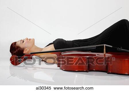 Stock Photography - Woman laying down on the floor alongside a cello. Fotosearch