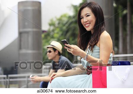Woman sitting outdoors with shopping bags using phone View Large Photo Image Picture - Woman sitting outdoors with shopping bags using phone. Fotosearch