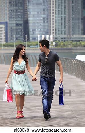 Stock Photo - Young couple holding hands walking together with shopping bags. Fotosearch