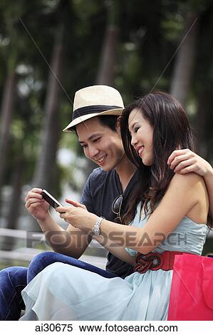 Stock Photography - Young couple looking at phone together outdoors. Fotosearch