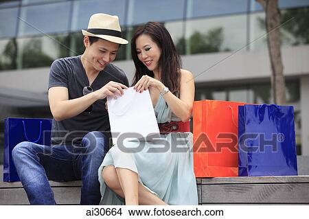 Young couple looking in shopping bags outdoors. View Large Photo Image Picture - Young couple looking in shopping bags outdoors.. Fotosearch