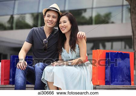 Stock Photograph - Young couple sitting outdoors with shopping bags.. Fotosearch